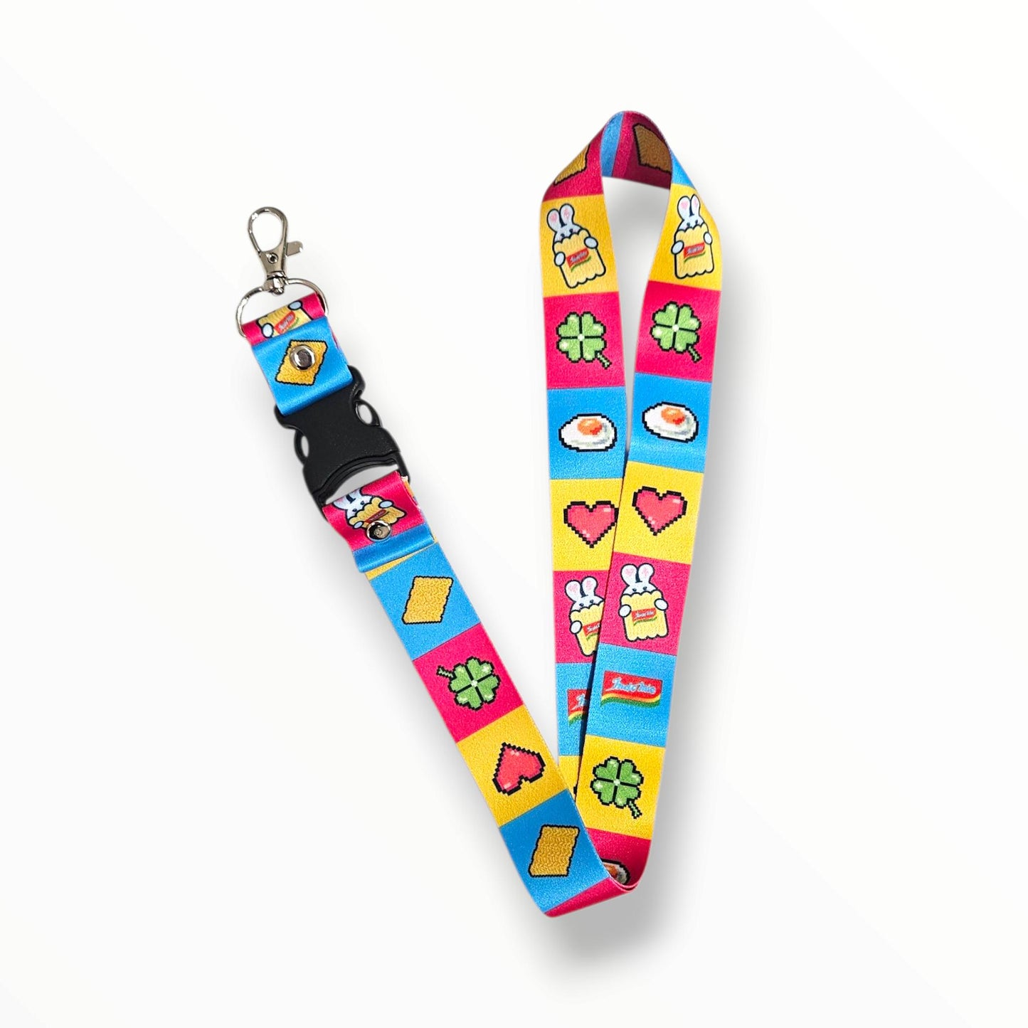 A colorful fabric lanyard with a metal clip and black plastic buckle, decorated with bright pink, blue, and yellow panels featuring cartoon-style icons such as hearts, clovers, fried eggs, and small character illustrations.